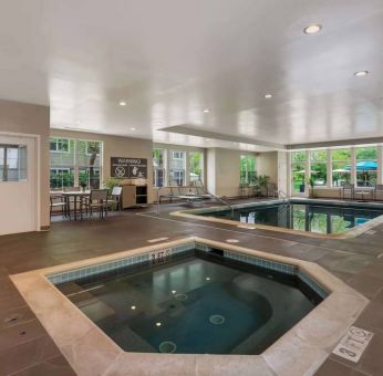 Sonesta ES Suites Parsippany Morris Plains’ indoor pool has a hot tub nearby, chairs and sun loungers nearby, and large windows.