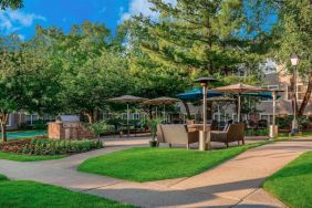 Sonesta ES Suites Parsippany Morris Plains’ barbecue area is furnished with tables and chairs, plus armchair seating, amid numerous trees.