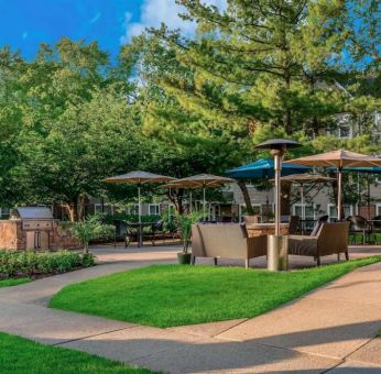 Sonesta ES Suites Parsippany Morris Plains’ barbecue area is furnished with tables and chairs, plus armchair seating, amid numerous trees.