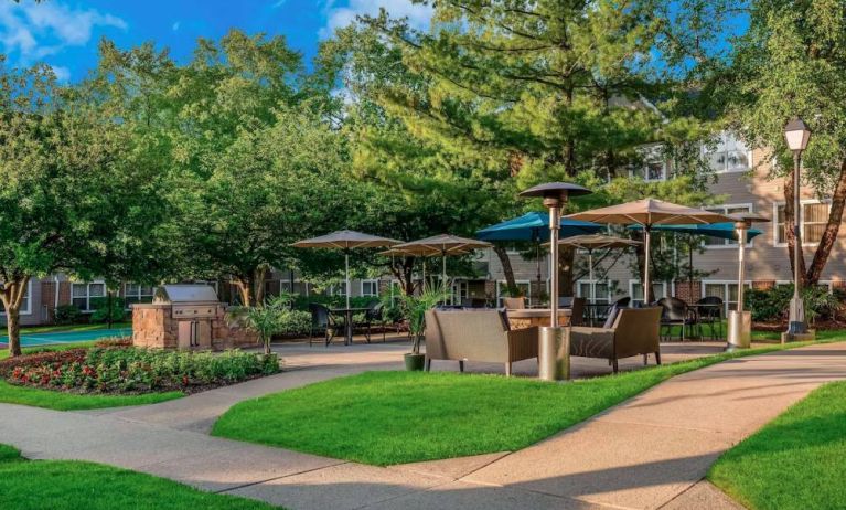 Sonesta ES Suites Parsippany Morris Plains’ barbecue area is furnished with tables and chairs, plus armchair seating, amid numerous trees.