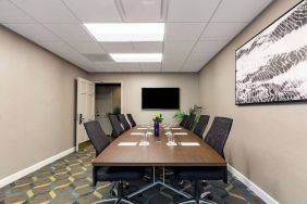 Hotel meeting room, featuring long wooden table, eight swivel chairs, and a large, widescreen TV on the wall.