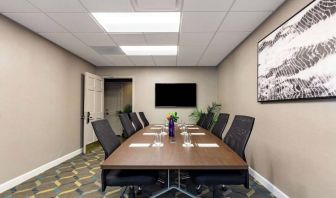 Hotel meeting room, featuring long wooden table, eight swivel chairs, and a large, widescreen TV on the wall.