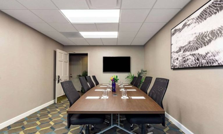 Hotel meeting room, featuring long wooden table, eight swivel chairs, and a large, widescreen TV on the wall.