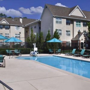 The outdoor pool of Sonesta ES Suites Birmingham Homewood is equipped with a lift, and both sun loungers and shaded tables/chairs are in the vicinity.