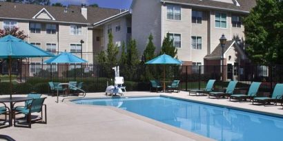 The outdoor pool of Sonesta ES Suites Birmingham Homewood is equipped with a lift, and both sun loungers and shaded tables/chairs are in the vicinity.