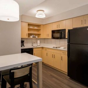 Sonesta ES Suites Andover Boston guest room kitchen, featuring oven, hob, microwave, fridge-freezer, and a kitchen table with two stools.