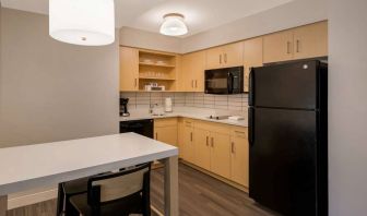 Sonesta ES Suites Andover Boston guest room kitchen, featuring oven, hob, microwave, fridge-freezer, and a kitchen table with two stools.