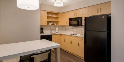 Sonesta ES Suites Andover Boston guest room kitchen, featuring oven, hob, microwave, fridge-freezer, and a kitchen table with two stools.