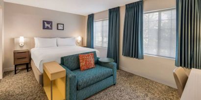 Sonesta ES Suites Andover Boston double bed guest room, including sofa, coffee table, and two windows.