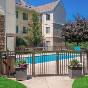 Sonesta ES Suites Andover Boston’s outdoor pool is ringed by a fence, with a backdrop of the hotel and numerous trees.