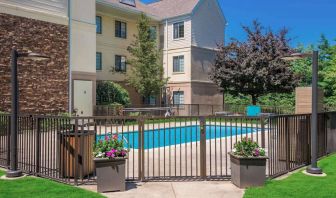 Sonesta ES Suites Andover Boston’s outdoor pool is ringed by a fence, with a backdrop of the hotel and numerous trees.