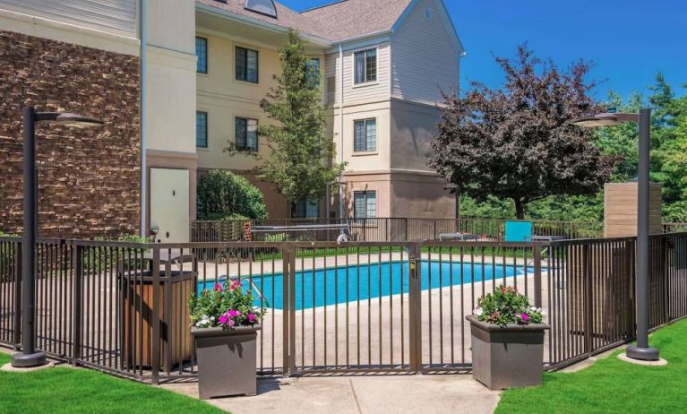 Sonesta ES Suites Andover Boston’s outdoor pool is ringed by a fence, with a backdrop of the hotel and numerous trees.