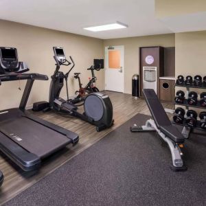 The fitness center in Sonesta ES Suites Andover Boston is equipped with rows of free weights, a bench, and a variety of exercise machines.