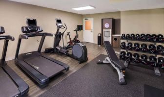 The fitness center in Sonesta ES Suites Andover Boston is equipped with rows of free weights, a bench, and a variety of exercise machines.