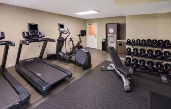 The fitness center in Sonesta ES Suites Andover Boston is equipped with rows of free weights, a bench, and a variety of exercise machines.