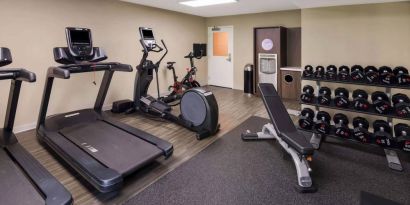 The fitness center in Sonesta ES Suites Andover Boston is equipped with rows of free weights, a bench, and a variety of exercise machines.