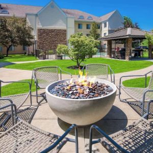 Sonesta ES Suites Andover Boston’s fire-pit is located amid pleasant greenery and surrounded by chairs, with the gazebo and barbecue facilities nearby.