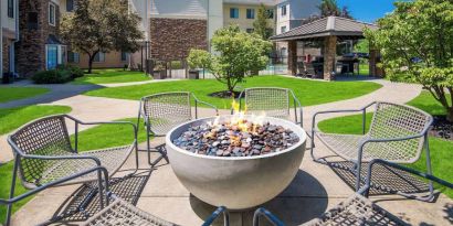 Sonesta ES Suites Andover Boston’s fire-pit is located amid pleasant greenery and surrounded by chairs, with the gazebo and barbecue facilities nearby.