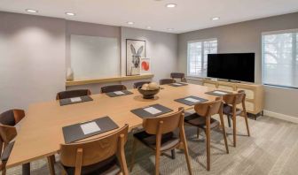 Hotel meeting room, with long wooden table and seating for nine, art and a whiteboard on the wall, and a large television. 