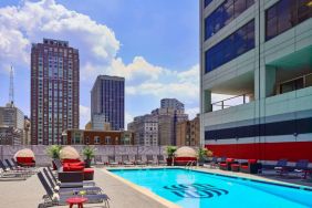 Sonesta Philadelphia Rittenhouse Square’s rooftop pool has sun loungers, armchairs, and potted plants by the side, addition to shaded seating.