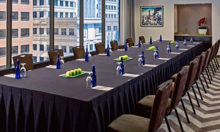 Sonesta Philadelphia Rittenhouse Square meeting room, featuring long table with space for over a dozen attendees, city views through the large windows, and art on the wall.