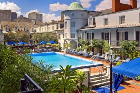 Royal Sonesta New Orleans’ outdoor pool has sun loungers by the side and shaded tables and chairs, and trees, nearby.