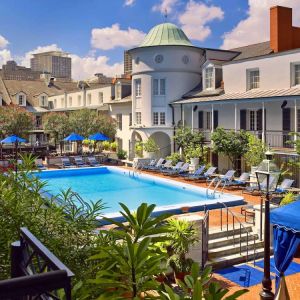 Royal Sonesta New Orleans’ outdoor pool has sun loungers by the side and shaded tables and chairs, and trees, nearby.