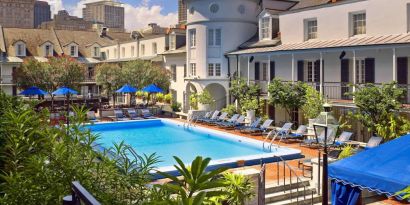 Royal Sonesta New Orleans’ outdoor pool has sun loungers by the side and shaded tables and chairs, and trees, nearby.