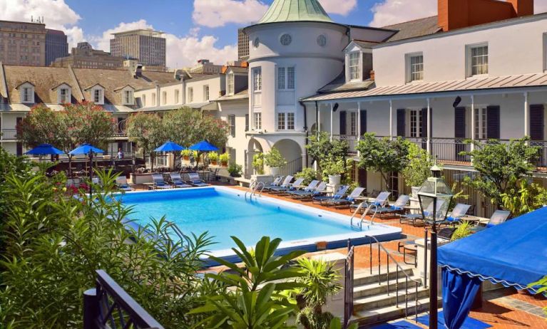 Royal Sonesta New Orleans’ outdoor pool has sun loungers by the side and shaded tables and chairs, and trees, nearby.