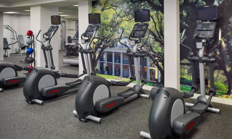 The fitness center in Royal Sonesta New Orleans is equipped with an assortment of exercise machines, and large images of greenery on the walls.