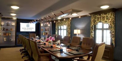 Meeting room in Royal Sonesta New Orleans, furnished with long wooden table, 14 swivel chairs, a widescreen TV, and two windows.