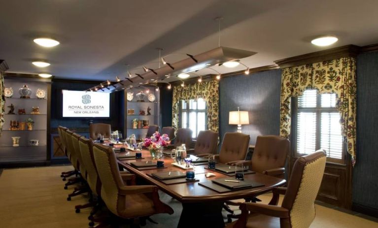 Meeting room in Royal Sonesta New Orleans, furnished with long wooden table, 14 swivel chairs, a widescreen TV, and two windows.