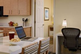 Guest room workspace in Sonesta ES Suites Atlanta - Perimeter Center North, featuring desk, chair, and lamp, next to the kitchen area.