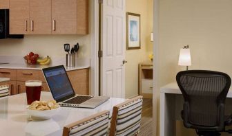 Guest room workspace in Sonesta ES Suites Atlanta - Perimeter Center North, featuring desk, chair, and lamp, next to the kitchen area.