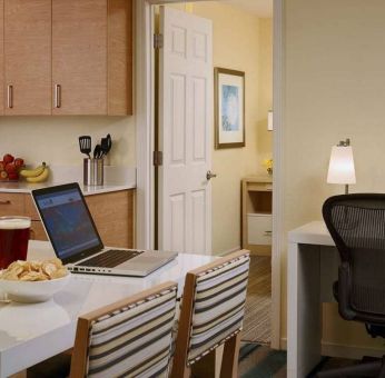 Guest room workspace in Sonesta ES Suites Atlanta - Perimeter Center North, featuring desk, chair, and lamp, next to the kitchen area.