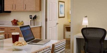 Guest room workspace in Sonesta ES Suites Atlanta - Perimeter Center North, featuring desk, chair, and lamp, next to the kitchen area.