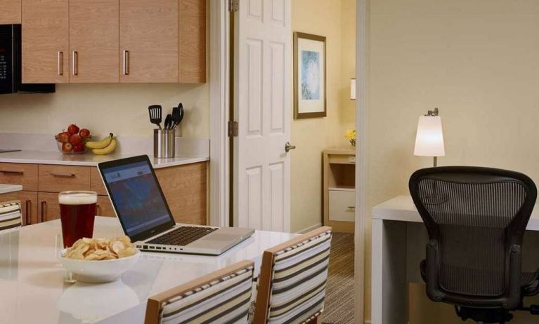 Guest room workspace in Sonesta ES Suites Atlanta - Perimeter Center North, featuring desk, chair, and lamp, next to the kitchen area.