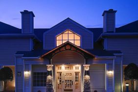 The hotel’s exterior has an entrance roof supported by rustic stonework pillars, with small trees on either side.