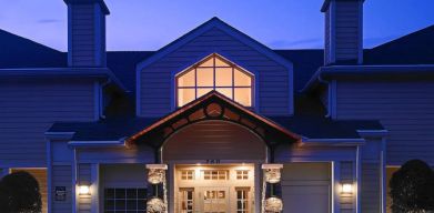 The hotel’s exterior has an entrance roof supported by rustic stonework pillars, with small trees on either side.