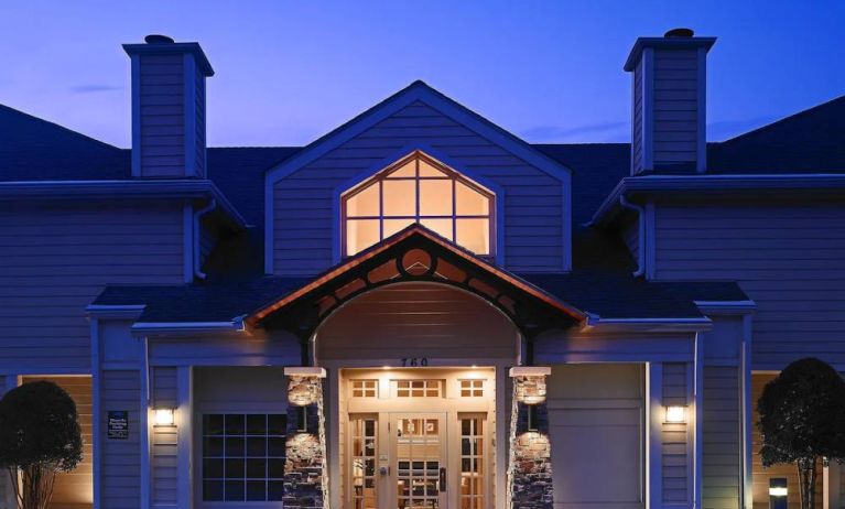 The hotel’s exterior has an entrance roof supported by rustic stonework pillars, with small trees on either side.