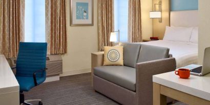 Sonesta ES Suites Auburn Hills Detroit double bed guest room, featuring table, chairs, windows, and a sofa.