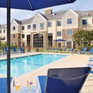 Sonesta ES Suites Auburn Hills Detroit’s outdoor pool has sun loungers, chairs, and small tables around it, with shade available.