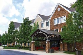 The hotel’s exterior features a covered entranceway with a pair of benches, flanked by numerous trees and bushes.