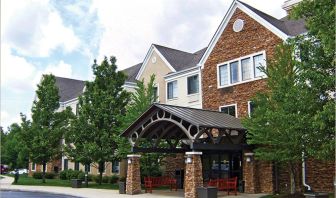 The hotel’s exterior features a covered entranceway with a pair of benches, flanked by numerous trees and bushes.