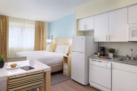 Sonesta ES Suites New Orleans double bed guest room, with nearby dining table and kitchen area, plus a large window.