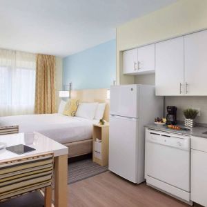 Sonesta ES Suites New Orleans double bed guest room, with nearby dining table and kitchen area, plus a large window.