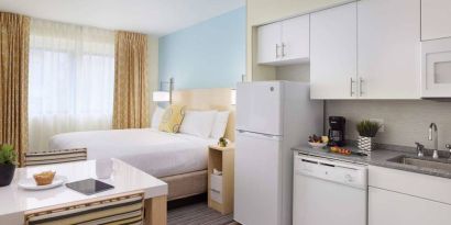 Sonesta ES Suites New Orleans double bed guest room, with nearby dining table and kitchen area, plus a large window.