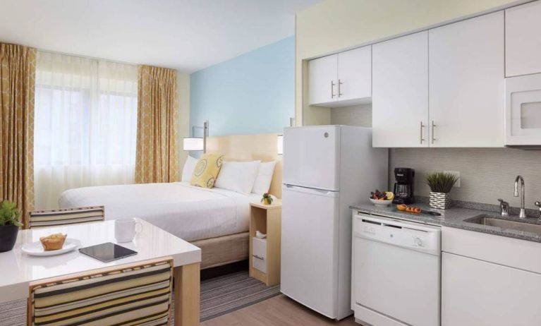 Sonesta ES Suites New Orleans double bed guest room, with nearby dining table and kitchen area, plus a large window.