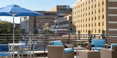 The rooftop terrace at Sonesta ES Suites New Orleans features armchairs and coffee tables, plus shaded tables and chairs, amid the fresh air.