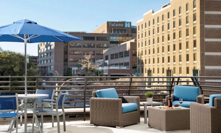 The rooftop terrace at Sonesta ES Suites New Orleans features armchairs and coffee tables, plus shaded tables and chairs, amid the fresh air.